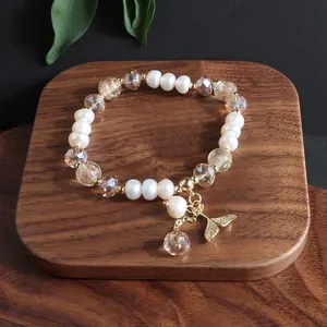 Nahaufnahme eines Naturperlenarmbands mit Kristallperlen und goldenem Fischschwanz-Anhänger