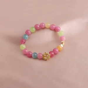 Nahaufnahme eines mehrfarbigen Edelstein-Armbands mit einem goldenen Blumenanhänger.