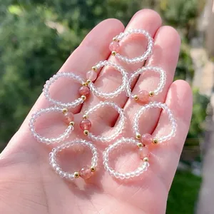 Detail von Erdbeerquarz- und Kristallperlen-Stretchringen, die in der Hand gehalten werden.