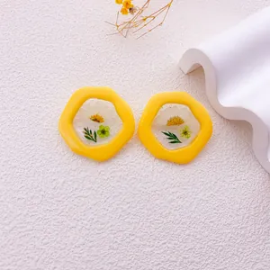 Primer plano de pendientes amarillos irregulares con flores de margarita secas reales.