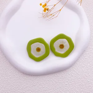 Primer plano de pendientes de resina verde con margaritas blancas secas en su interior