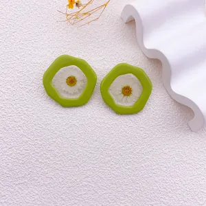 Primer plano de aretes verdes irregulares con flores de margaritas blancas secas