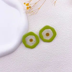 Primer plano de pendientes verdes irregulares con margaritas blancas secas reales.