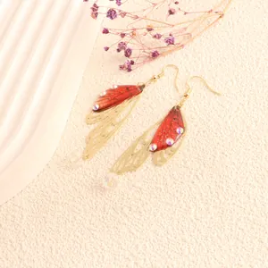 Close-up of fairy butterfly wing earrings with red resin and golden metal filigree detail