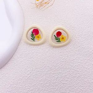 Detalle de pendientes triangulares de resina con flores secas reales rojas y amarillas.