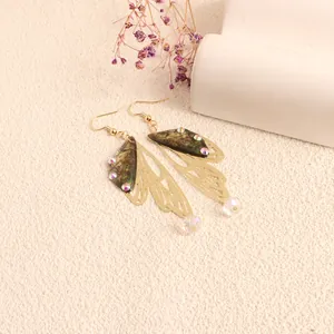 Detailed view of long gold filigree butterfly wing earrings with iridescent rhinestones.