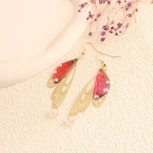 Close-up of red butterfly wing drop earrings with gold trim and crystal accents