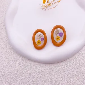 Detalle macro de pendientes naranjas con flores secas reales violetas y amarillas incrustadas