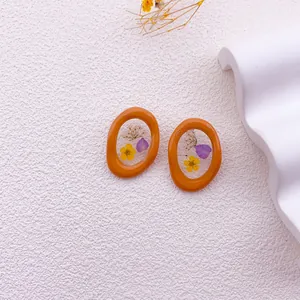 Detalle de pendientes ovalados irregulares con flores secas reales amarillas y lilas