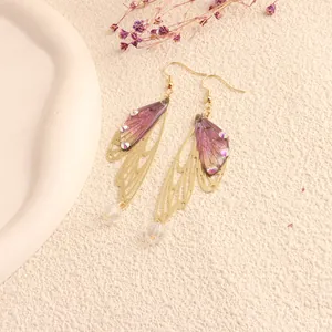 Detail view of purple simulated cicada wing earrings with gold metal frame and rhinestones