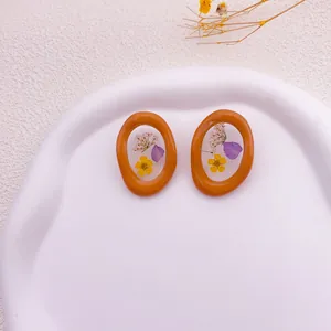 Vista detallada de pendientes de resina naranja con flores secas reales encapsuladas.