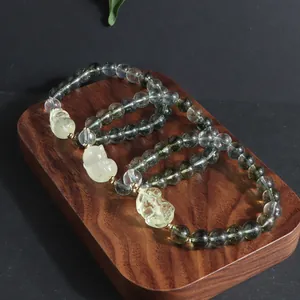 Close-up detail of Green Ghost crystal bracelets with yellow carved lion pendants on wood