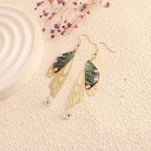 Detailed view of iridescent green cicada wing drop earrings with gold hollow design
