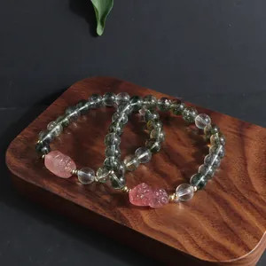 Elegant Green Ghost and Strawberry Quartz bracelets with lion charms on wood stand.