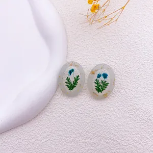 Detalle de pendientes ovalados de resina con flores secas azules y pan de oro