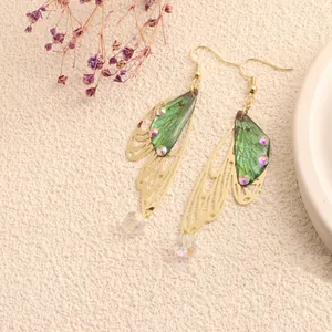 Close-up of elegant gold butterfly wing earrings with green details and shiny crystals.