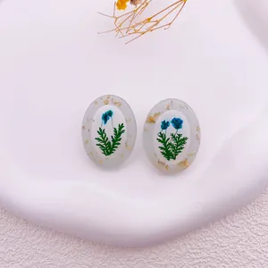 Detalle de pendientes ovalados de resina con flores secas azules y copos de pan de oro