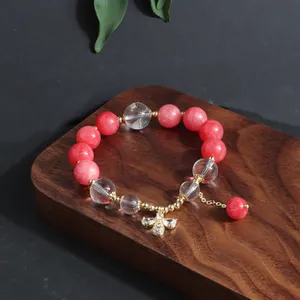 Detailansicht eines Armbands mit rosa und klaren Perlen und Bienenanhänger auf Holz