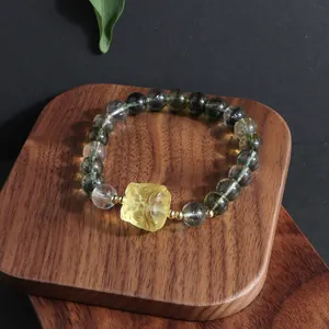 Macro shot of a green phantom crystal bead bracelet featuring a carved yellow floral charm.