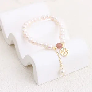 Macro shot of a freshwater pearl bracelet with a gold Fu character charm.