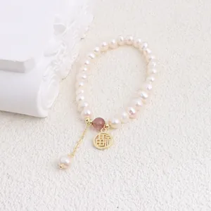 Close-up of freshwater pearl bracelet featuring a golden Fu character charm and red bead.