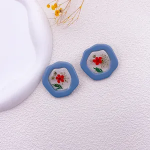 Vista detallada de pendientes azules irregulares con flores secas rojas reales dentro.