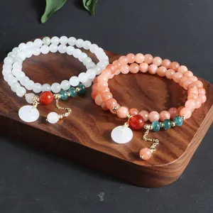 Primer plano de pulseras vintage de piedra natural con colgante Ping'an Kou sobre madera.