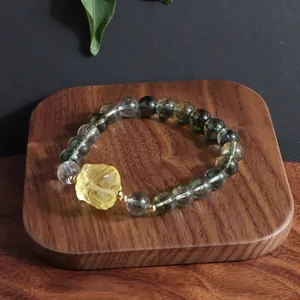 Detail of a green phantom crystal bracelet with a yellow carved flower charm on wood