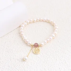 Close-up detail of a natural freshwater pearl bracelet featuring a gold Fu character charm and pink stone