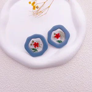 Primer plano de pendientes azules irregulares con flores secas reales en resina transparente.
