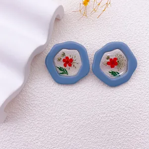 Primer plano de pendientes de resina azul con flores secas rojas naturales y hojas incrustadas