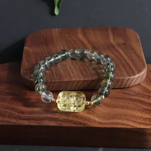Detailed view of a green phantom quartz bracelet with a yellow lion plate on wood