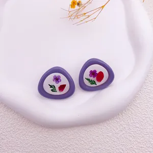 Primer plano de pendientes morados irregulares con flores secas reales y hojas verdes naturales