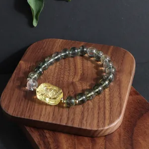 Close-up of Green Phantom crystal bracelet with a carved lemon yellow charm on wood.