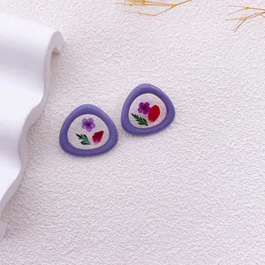 Primer plano de pendientes geométricos morados con flores y hojas secas reales.