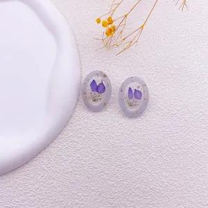 Detalle de pendientes de resina con flores secas púrpuras reales y láminas de oro.