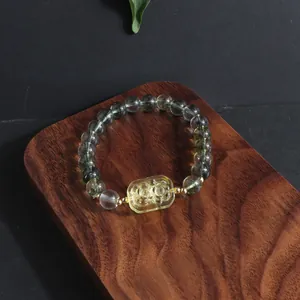 Macro detail of Green Ghost crystal bracelet with carved yellow dancing lion on wood