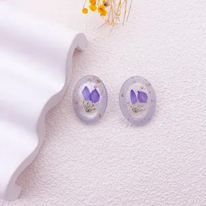 Detalle macro de elegantes pendientes ovalados de resina con pétalos de flores púrpuras y pan de oro