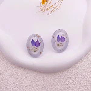 Primer plano de pendientes de resina hechos a mano con flores secas moradas y oro