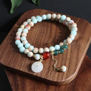 Detalle de una pulsera de varias vueltas de piedra natural con colgante de hebilla de paz de jade.