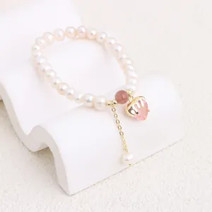 Close-up of freshwater pearl bracelet with a pink heart-shaped crystal charm and gold chain.