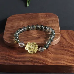 Detail shot of a green phantom quartz bracelet with a yellow crystal lion pendant on wood