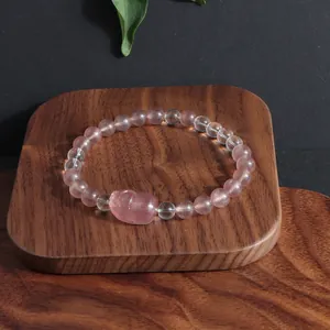 Vue détaillée d'un bracelet Pixiu en quartz fraise sur un support en bois naturel