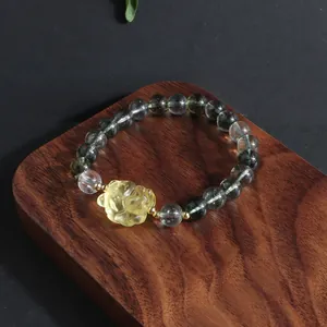 Detail view of a green phantom crystal bracelet with a yellow carved lion head on wood.
