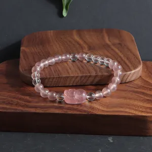 Détail en gros plan du bracelet en quartz fraise et cristal Pixiu sur socle en bois
