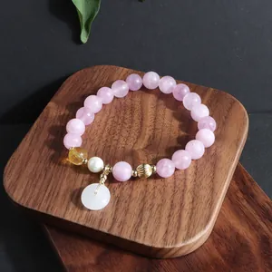 Nahaufnahme eines Armbands aus rosa Kristall mit weißem Jade-Anhänger und Perlenakzenten