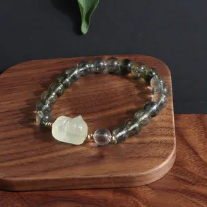 Detailed close-up of a green phantom quartz bracelet with a yellow charm on wood