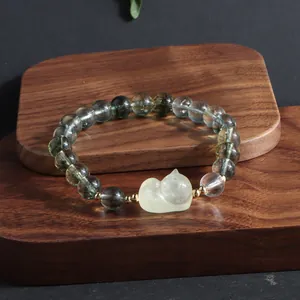 Detail shot of a green phantom crystal bracelet with a cute yellow fox charm on dark wood