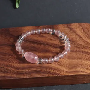 Gros plan d'un bracelet en quartz fraise avec un charme Pi Xiu sur une surface en bois.