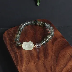 Close-up of a green ghost quartz bracelet with a carved lion charm on a wooden stand.